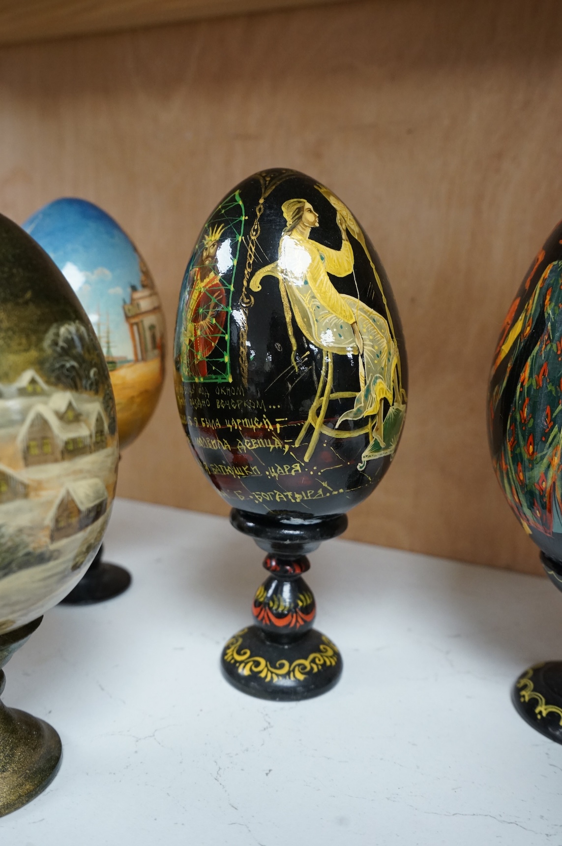 Five Russian painted and lacquered 'eggs' on stands, one inscribed in cyrillic, largest 21cm high